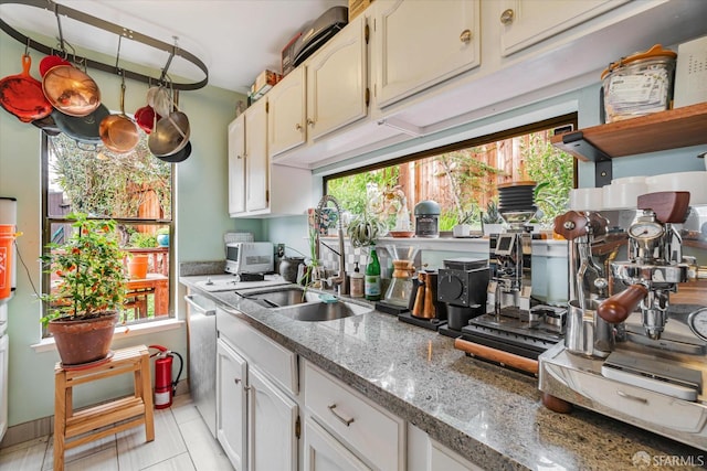 kitchen with light stone counters, stainless steel dishwasher, white cabinets, a sink, and light tile patterned flooring