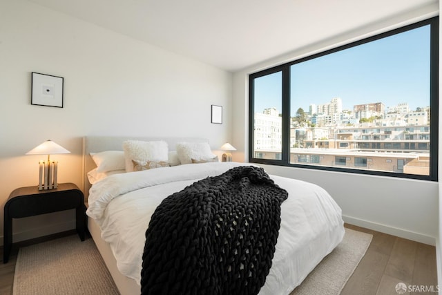 bedroom featuring a view of city, wood finished floors, and baseboards