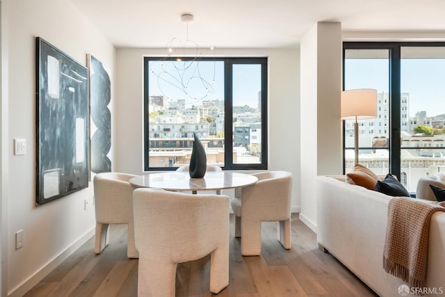 dining space featuring light wood-type flooring, a healthy amount of sunlight, a city view, and a notable chandelier