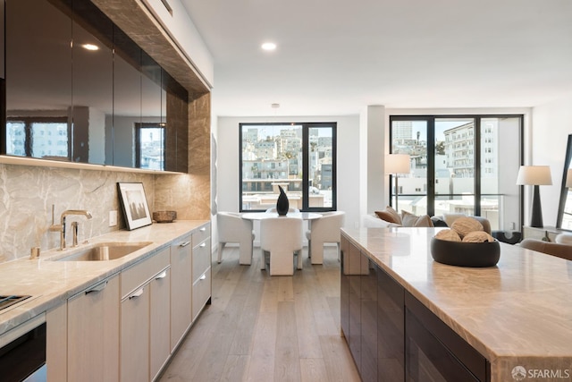 kitchen with wall oven, tasteful backsplash, open floor plan, light wood-type flooring, and a sink