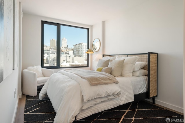 bedroom featuring a view of city, baseboards, wood finished floors, and multiple windows