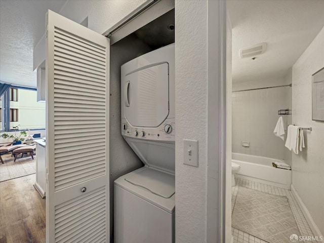 washroom with hardwood / wood-style floors, a textured ceiling, and stacked washer and clothes dryer