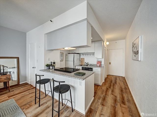 kitchen featuring white cabinets, kitchen peninsula, light wood-type flooring, and black appliances