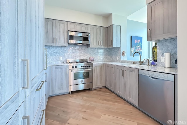 kitchen with sink, gray cabinetry, stainless steel appliances, light stone countertops, and light hardwood / wood-style floors