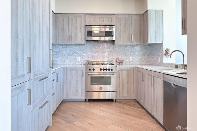 kitchen featuring tasteful backsplash, sink, light hardwood / wood-style floors, stainless steel appliances, and light stone countertops