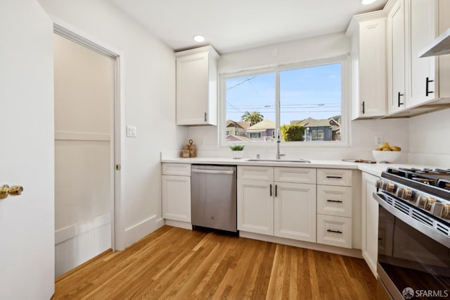 kitchen with white cabinets, stainless steel appliances, light countertops, light wood-style floors, and a sink