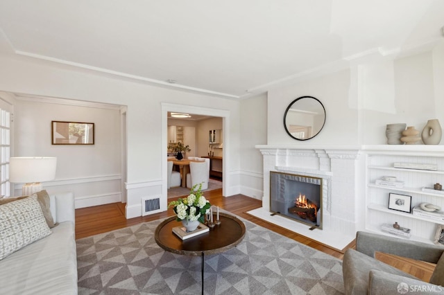 living room featuring a fireplace with flush hearth, visible vents, and wood finished floors