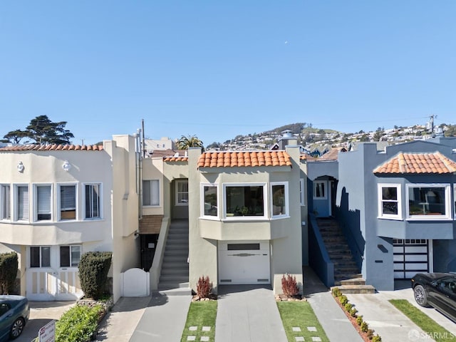 view of front facade featuring a tile roof, driveway, stairway, and stucco siding