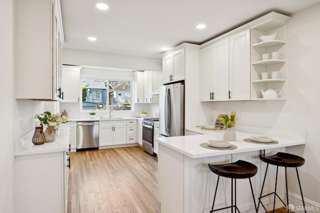 kitchen with open shelves, appliances with stainless steel finishes, white cabinetry, light wood-type flooring, and a peninsula