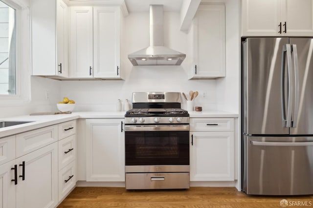 kitchen with stainless steel appliances, wall chimney range hood, light countertops, and white cabinets