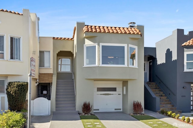 mediterranean / spanish-style home featuring a garage, concrete driveway, a tiled roof, stairs, and stucco siding