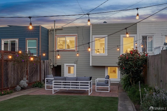 back of property at dusk featuring a yard, a patio area, fence, and an outdoor living space