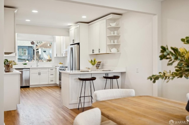 kitchen with a peninsula, white cabinets, appliances with stainless steel finishes, open shelves, and light wood finished floors