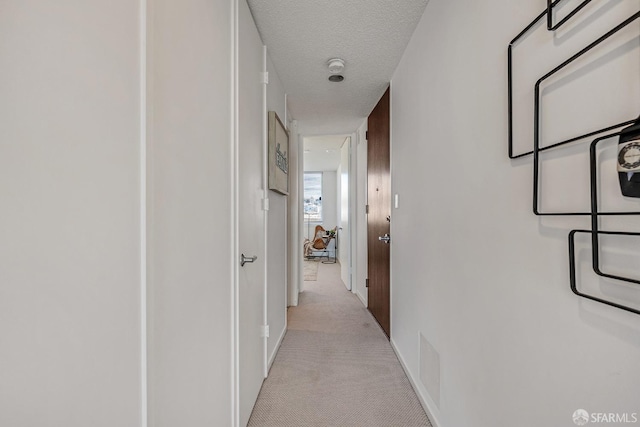 hall featuring a textured ceiling and light colored carpet