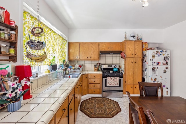 kitchen featuring white refrigerator, stainless steel range oven, sink, decorative backsplash, and tile countertops