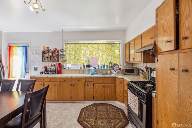 kitchen featuring tasteful backsplash, tile countertops, ventilation hood, stainless steel range with gas cooktop, and an inviting chandelier