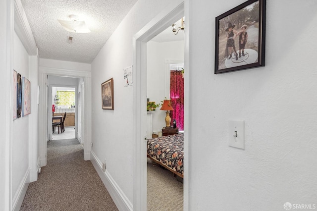 hallway featuring carpet floors, a textured ceiling, and a notable chandelier