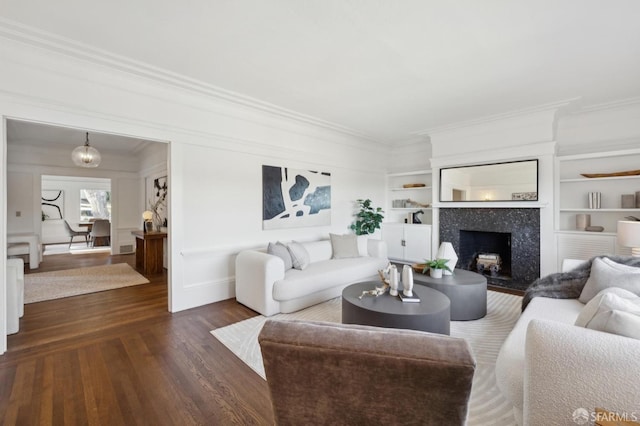 living room with built in shelves, a fireplace, ornamental molding, and dark hardwood / wood-style flooring