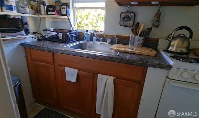 kitchen featuring dark countertops, brown cabinets, a sink, and white gas range oven