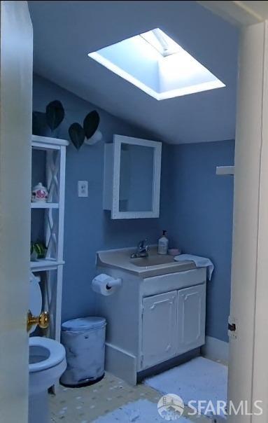 half bath featuring toilet, lofted ceiling with skylight, and vanity