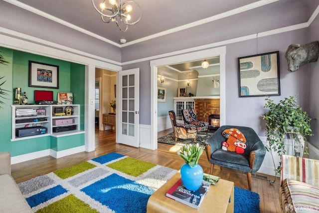 living room with ornamental molding, wood finished floors, french doors, a lit fireplace, and a chandelier