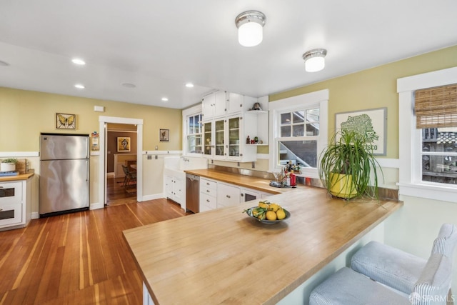 kitchen featuring a peninsula, wood finished floors, white cabinets, stainless steel appliances, and open shelves