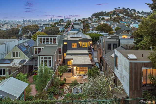 back of house at dusk with roof mounted solar panels, a city view, a deck, and fence