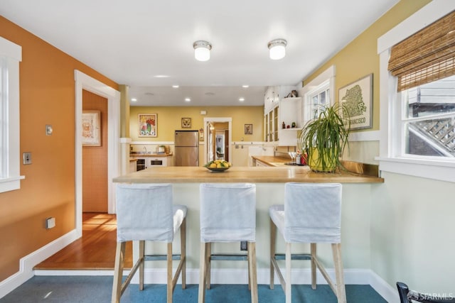 kitchen with baseboards, a kitchen bar, recessed lighting, a peninsula, and freestanding refrigerator