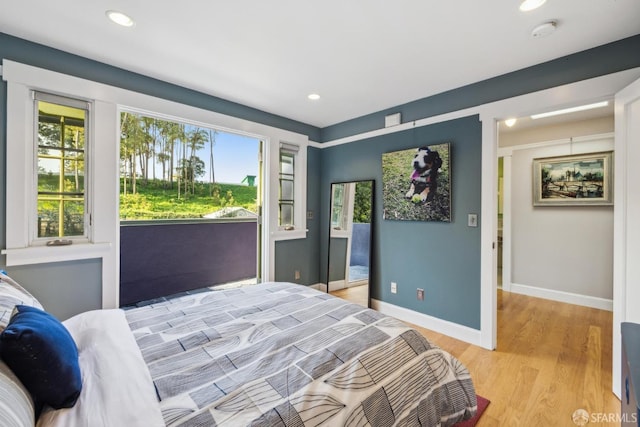 bedroom featuring multiple windows, baseboards, light wood-style floors, and access to outside