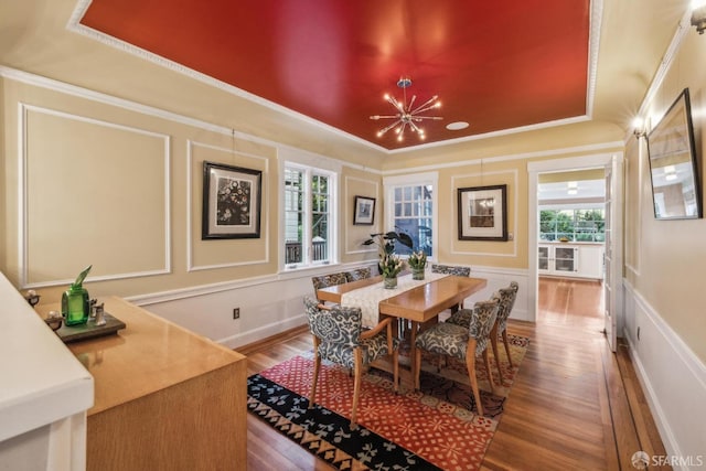 dining space with a decorative wall, a tray ceiling, ornamental molding, wood finished floors, and a notable chandelier