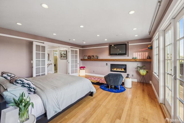 bedroom with a glass covered fireplace, recessed lighting, french doors, and light wood-style floors