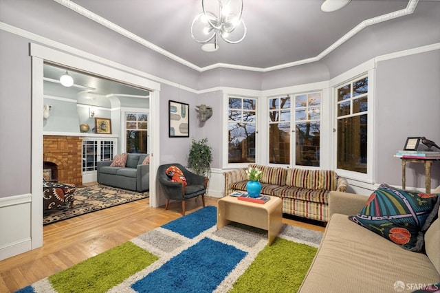 living area featuring crown molding, a brick fireplace, a notable chandelier, and wood finished floors