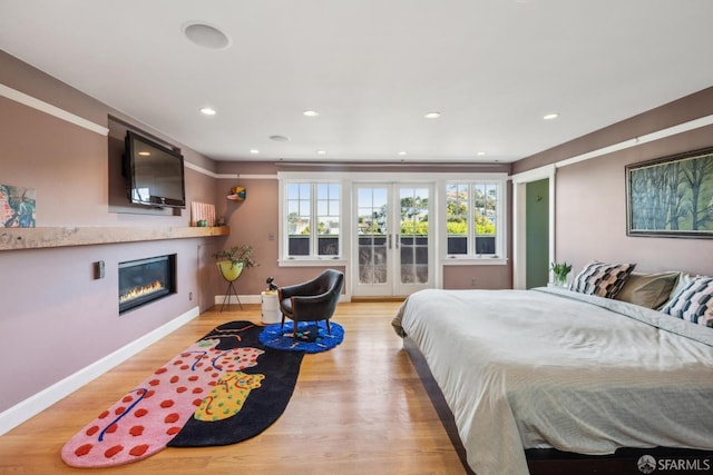 bedroom featuring baseboards, light wood-type flooring, french doors, a glass covered fireplace, and access to outside