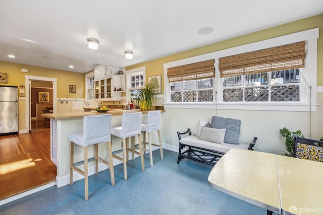 kitchen with baseboards, a breakfast bar, a peninsula, recessed lighting, and freestanding refrigerator