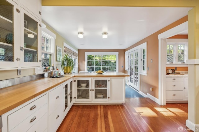 kitchen featuring glass insert cabinets, white cabinets, wood finished floors, and a peninsula