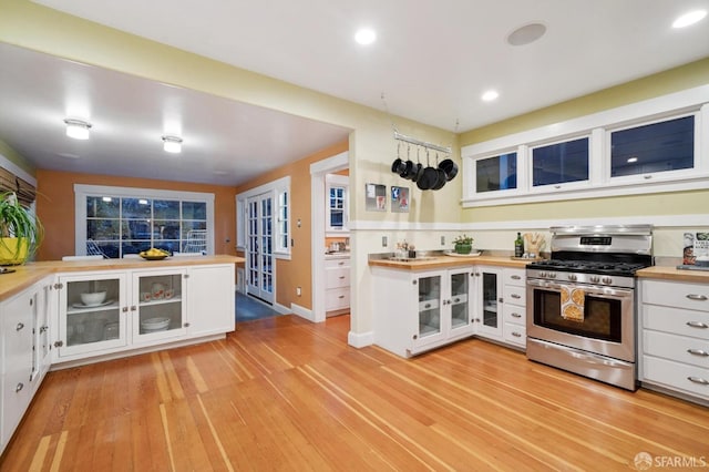 kitchen featuring gas range, white cabinets, light wood-style flooring, and wood counters