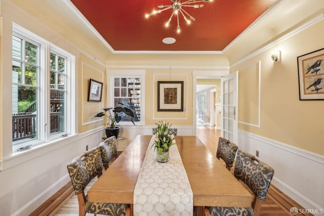 dining area with a raised ceiling, wood finished floors, baseboards, and ornamental molding