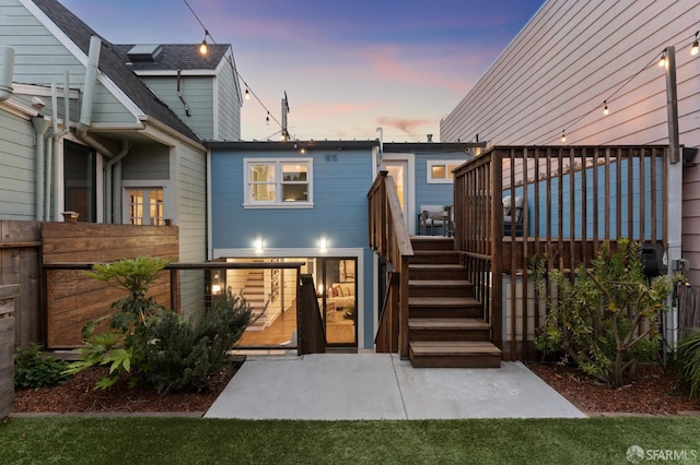 back of property at dusk with stairway, a deck, and fence