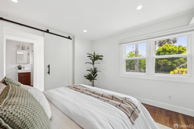 bedroom with a barn door, baseboards, wood finished floors, recessed lighting, and ensuite bath