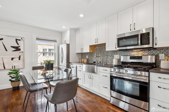 kitchen featuring stainless steel appliances, dark countertops, a sink, decorative backsplash, and white cabinets