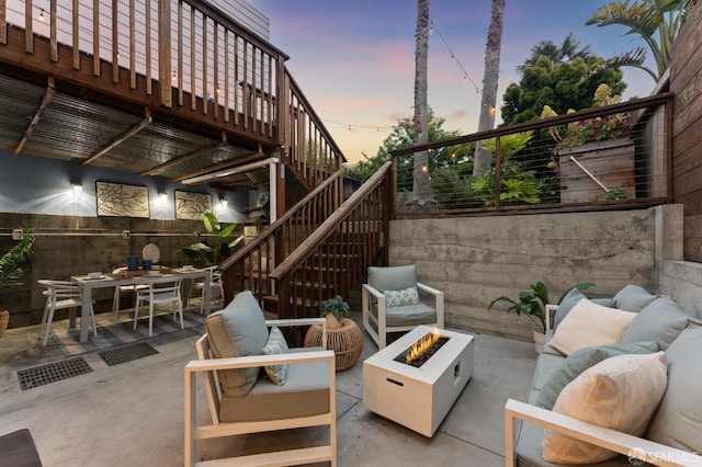 patio terrace at dusk with an outdoor living space with a fire pit, outdoor dining space, stairs, and fence