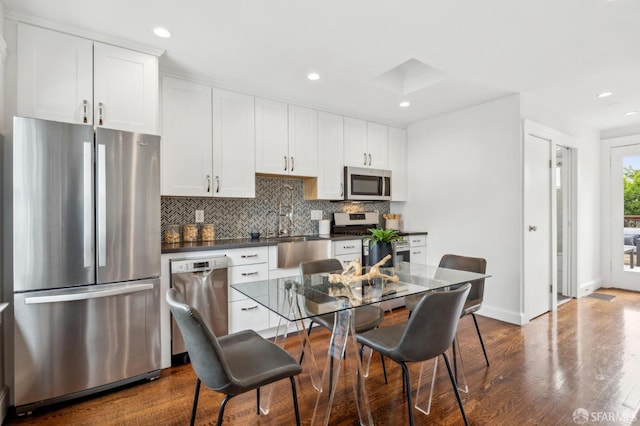 kitchen with stainless steel appliances, dark countertops, tasteful backsplash, dark wood-style floors, and white cabinetry