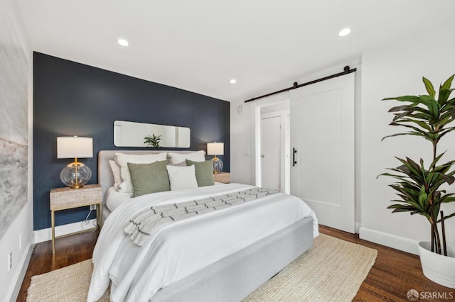 bedroom featuring a barn door, wood finished floors, baseboards, an accent wall, and recessed lighting