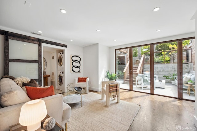 living area with stacked washer and clothes dryer, a barn door, wood finished floors, recessed lighting, and baseboards