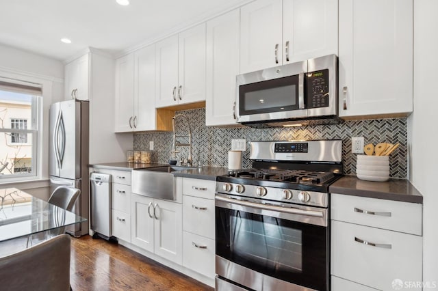 kitchen featuring stainless steel appliances, dark countertops, a sink, white cabinetry, and recessed lighting