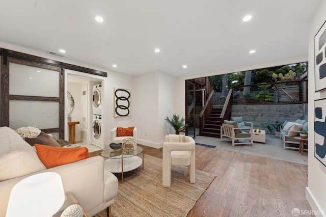 living room featuring estacked washer and dryer, a barn door, wood finished floors, recessed lighting, and stairs