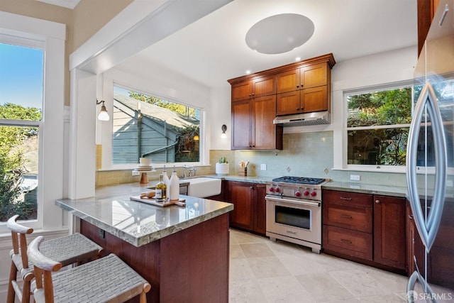 kitchen with kitchen peninsula, a kitchen breakfast bar, appliances with stainless steel finishes, sink, and tasteful backsplash