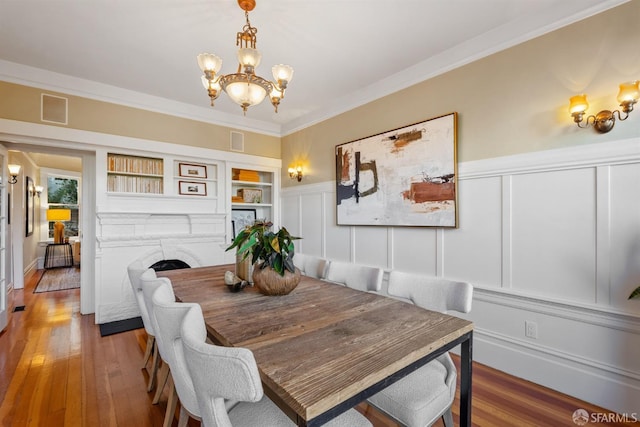 dining area featuring built in features, hardwood / wood-style floors, a chandelier, and ornamental molding