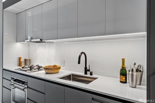 kitchen featuring oven, stainless steel gas stovetop, gray cabinetry, and sink