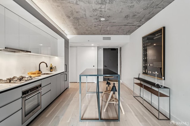 kitchen featuring gray cabinetry, sink, light wood-type flooring, range hood, and stainless steel appliances